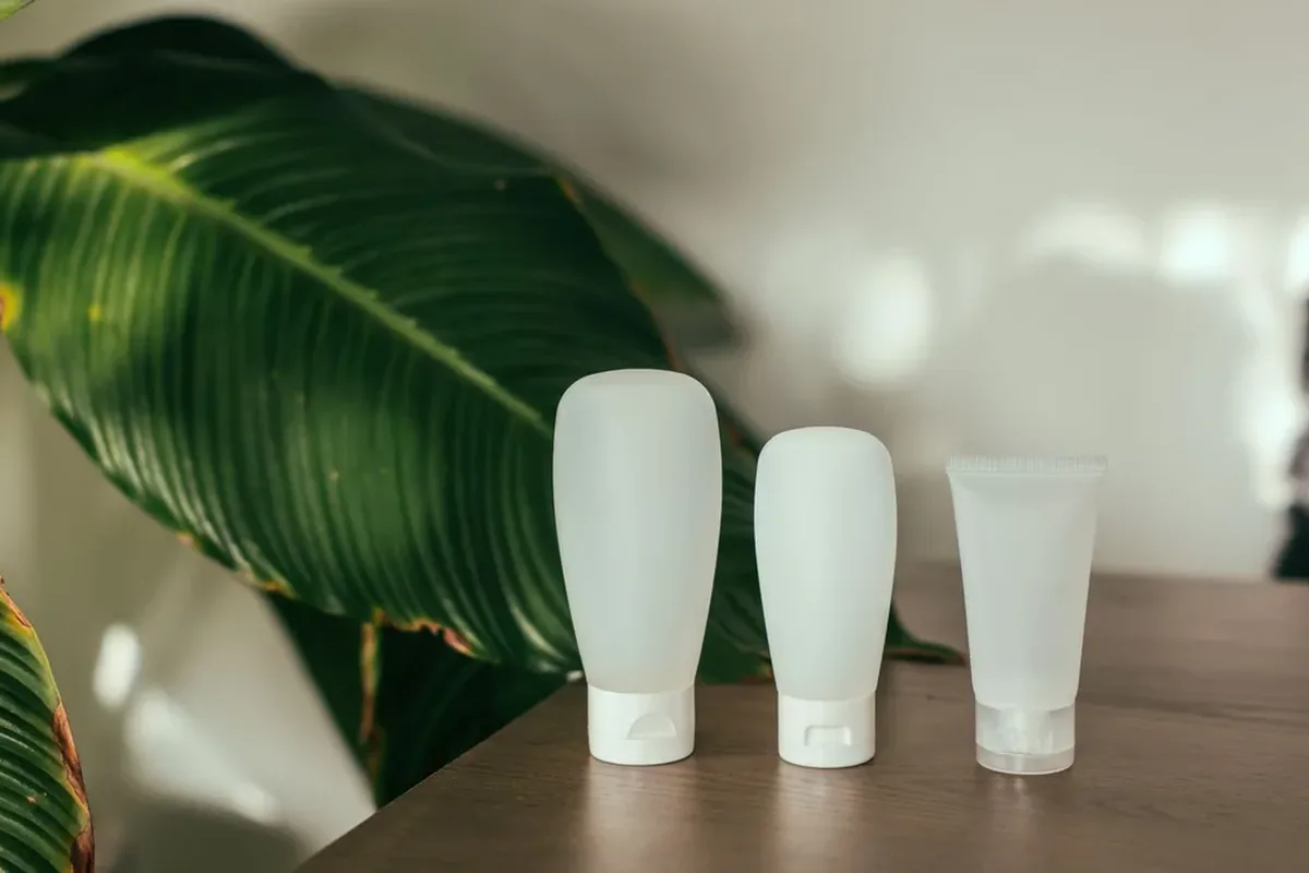 Three unlabelled white cosmetic tubes standing on a wooden table beside a leafy plant